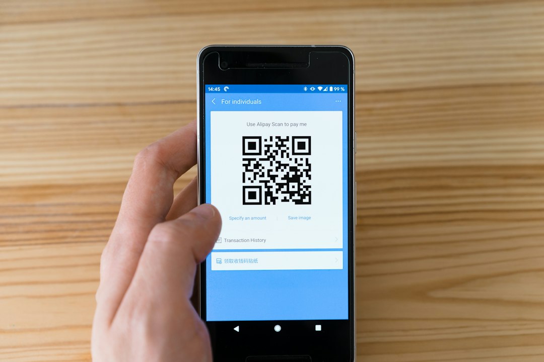 Mão segurando smartphone com QR Code na tela sobre mesa de madeira